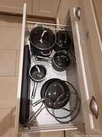 Overhead view of four pots with lids and two pans stored in kitchen drawer