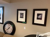 View of two framed black and white prints on wall and large round clock below them.