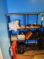 Metal frame shelving unit with wooden shelves against a blue wall, showing some surrounding items for scale and context.