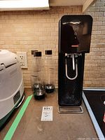 Full view of SodaStream dispenser unit alongside three transparent carbonation bottles with black caps.