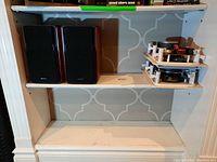 Four speakers on shelf; left side two Edifier bookshelf speakers, right side two wall insert speakers with exposed internal components