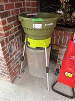 Front left view of SunJoe electric leaf mulcher showing the green hopper, yellow unit, metal stand legs, and translucent collection bag.