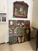 Nine tin flower and insect tiles arranged in a grid below wooden Molsons sign