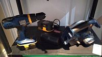 Photo showing Ryobi P206 drill, batteries, charger, and Ryobi P501 circular saw on shelf.