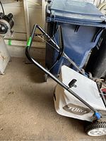 Side view of mower handle and attached cloth grass collection bag, in garage setting