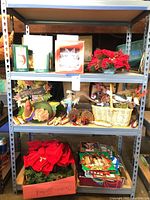 Three retail shelves filled with assorted holiday decorations including gift wrap, artificial poinsettia, red bow, decorative baskets and seasonal figurines.
