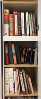 Cookbooks and binders are on shelves showing colorful hardbound cookbook spines and multiple binders in black, orange, blue and white on the middle shelf.
