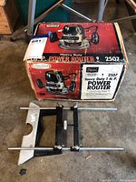 Front and side view of Craftsman Commercial Heavy Duty Power Router in original box alongside adjustable guide attachment laid out on floor.