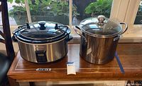 Photo of Cook 5 quart slow cooker and stainless steel stock pot with glass lid on a wooden table near window.