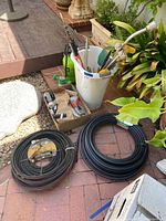 Overview of garden hoses coiled on ground next to plastic container with gardening tools and sprayer