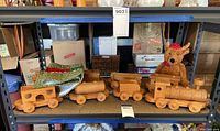 Full view of hand-made wooden train set with four connected pieces on a shelf alongside a stuffed teddy bear and cloth decoration.