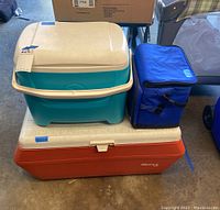 Three ice chests stacked: turquoise and white Igloo, blue soft cooler, and large orange Gott 80 cooler