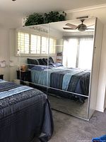 Two connected wardrobe units with mirrored doors in bedroom, reflecting bed and window.