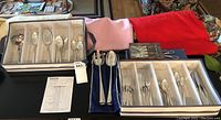 Wide view showing multiple fabric organizer trays holding various flatware pieces including spoons, forks, knives, and serving utensils, plus a boxed knife set and a pair of scissors on the table.