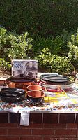 Photo of all pans and bakeware arranged on a tiled table outdoors with greenery background, showing the variety and quantity of items in the lot.