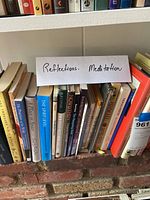 Books on a shelf with a handwritten sign 'Reflections Meditation' showing a mix of hardcover and paperback books, some titles visible.