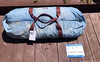 Blue canvas carrying bag with brown leather straps laying on wood deck, labeled with size 11'x11' and description screened canopy.