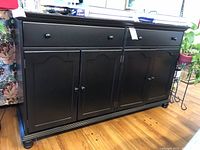 Front view of black wooden sideboard with two drawers and two cabinets, showing round knob handles and panel design.