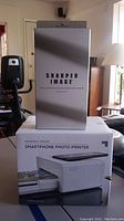 Box displaying Sharper Image branding and product photo of smartphone photo printer