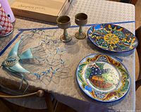 Lot items displayed on table: two painted Talavera plates, two pottery goblets, and metal fish wall art sculpture