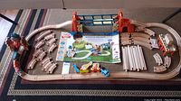 Full layout of wooden railway track assembled in a large oval with a red and blue suspension bridge in the center, two colorful wooden trains, and the Misty Island Adventure set box in the middle.