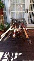 Front view of metal wheelbarrow loaded with assorted yard tools including rakes, broom, hammer, and shovel.