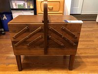 Front view of closed wooden sewing box on legs showing cantilever hinge detail