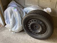 Three Motomaster winter tires on black steel rims with one tire facing forward showing tread and rim, others covered in plastic bags beside it