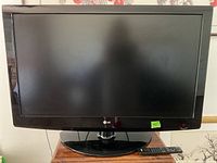 Front view of 42-inch LG TV showing screen, bezel, swivel base, and remote control on a wooden surface