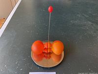 Two orange spherical salt and pepper shakers facing each other on a round metallic base with central pole, viewed from an angle showing the whole setup