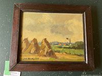 Overall view of framed oil painting showing haystacks, field, village spire under cloudy sky