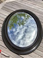 Top-down image of antique oval beveled mirror on wooden deck reflecting sky