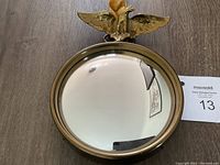Full view of the round convex mirror with brass frame and eagle topper, hanging by velvet ribbon.