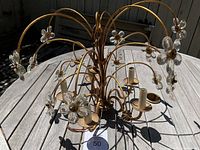 Overall front view of brass floral chandelier with curved arms and crystal petals, resting on wooden table.