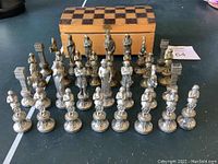 Full front view of all chess pieces arranged in rows in front of the storage box with checkerboard lid.