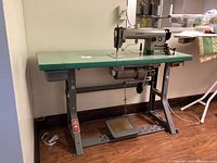 Full view of sewing machine on green tabletop and steel stand with foot pedal.