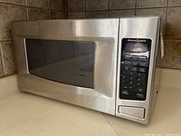 Front angled view of stainless steel KitchenAid microwave highlighting keypad on right side and door with mesh window
