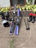 Full lot view showing two pairs of skis, two pairs of boots, ski poles and helmet.