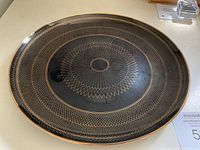 Black glass platter with detailed gold geometric designs shown from an angled top view.