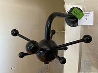 Photo showing side angle of the black metal coat rack with round ball hooks, mounted on a white wall near a column, with a green tag showing dimensions 10x15.