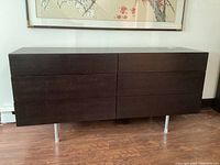 Front view of the dresser showing six drawers and chrome legs on a hardwood floor.