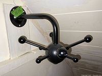 View showing one black Sputnik coat rack mounted on a white wooden wall with 7 spokes, one spoke missing.