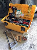 Yellow toolbox open showing cordless drill, screwdrivers, hand tools, drill bits, screws and wall plugs.
