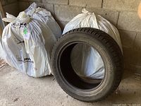 Four Yokohama tires, one outside of its protective white plastic bag, set near a concrete wall in a garage.
