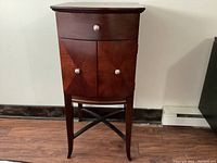 Front view of small wooden cabinet showing one drawer and two doors with round metal knobs. Dark wood finish visible.