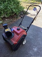 Front three-quarter view showing red housing, chute outlet, white wheels and black handle