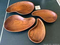 Four vintage hand-carved wood bowls with organic kidney shapes laid out on a black tabletop. Visible attractive wood grain and smooth finish. Two repaired cracks noticeable on close inspection.
