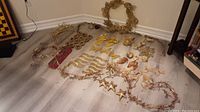 Photo showing assorted gold Christmas decorations including wreaths, star garlands, butterflies, angels, and other decorative items spread on floor.