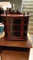 Closed view of the wooden decorative cabinet with glass door and side shelves, showing scratches and finish wear.