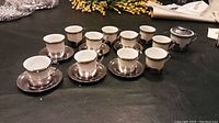Full set of espresso cups and saucers with sugar bowl displayed on black surface.